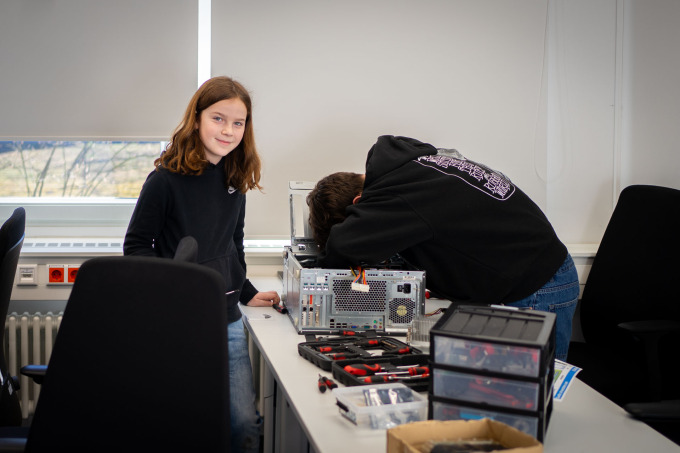 Zwei Schüler arbeiten an einem PC während einer freundlich in die Kamera lächelt