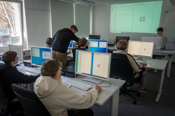 Ein Auszubildender erklärt einem Schüler eine Aufgabe während 4 weitere Schüler Aufgaben bearbeiten